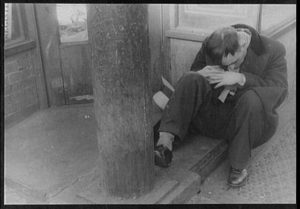 Man sitting on the ground, knees up, providing a little support as he sleeps off a drunk.